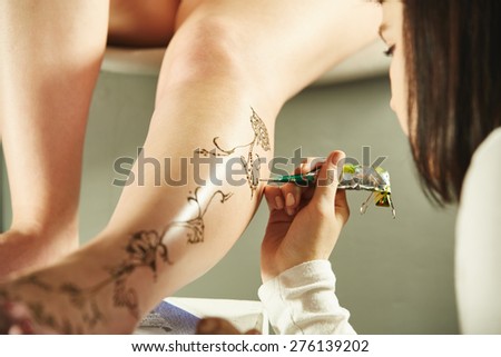 Master drawing with henna on leg of model