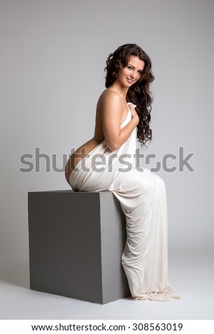 Smiling nude brunette posing sitting on cube