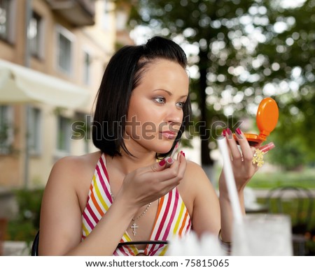 young beauty girl in summer cafe applying cosmetics looking at mirror