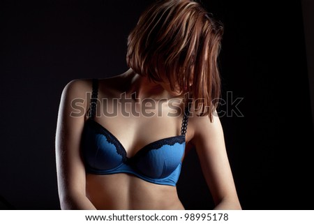 Young woman in blue lingerie hide face by hairs posing in dark