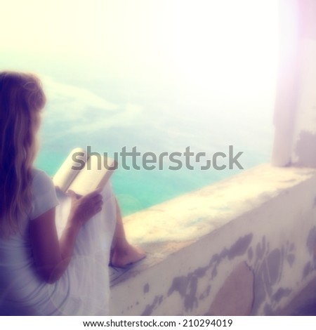 Relaxed blurry blonde woman reading a book outside. Light filter effect added.