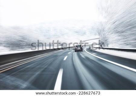 Blurry fast turn at the icy snow road with one car in the foreground. Motion blur visualizies danger of the high speed and dynamics.
