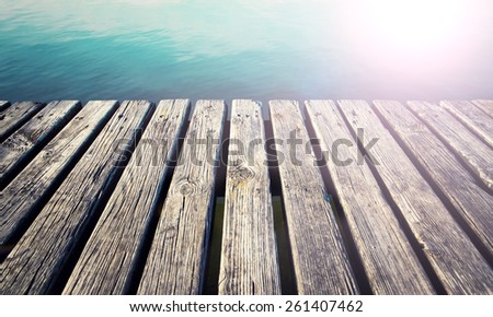 Aged sunny wooden lake pier with small waves on the lake and added bright light.