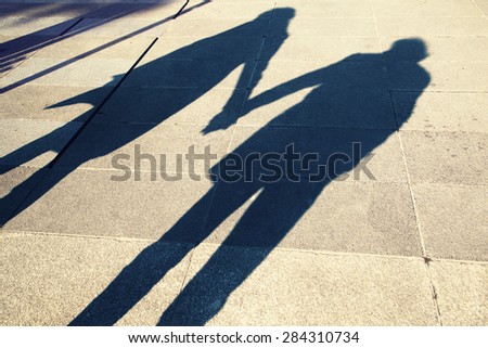 Shadow of two people holding hands on a walk in the city background, silhouette of two adult (girl and boy) holding hands at Sunset light. Two young people love each other.