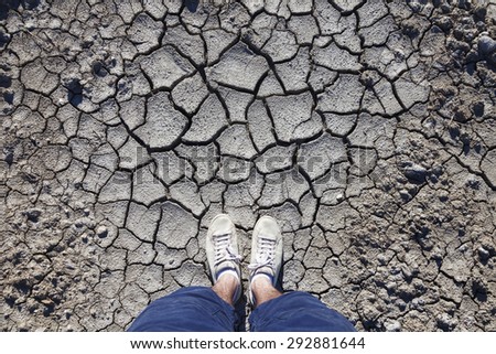 Man with white shoes standing on cracked dried soil ground. Concept photo. Point of view man standing on cracked soil ground.