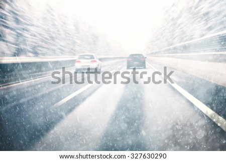 Blurry dangerous car overtaking on highway at heavy snowy conditions. Motion blur visualizies the speed and dynamics. Danger and fast speed driving at the heavy snowy and icy road.