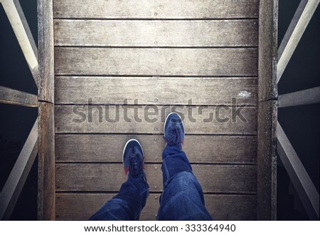 A man walking on aged wooden floor, point of view perspective. A man with blue shoes and jeans walking alone on old wooden bridge. Conceptual photo, point of view perspective used.