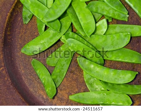 Freshly washed snow peas scattered on brown textured tray