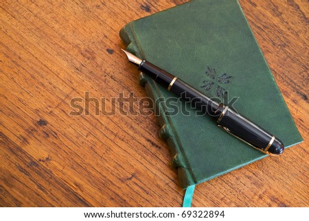 A leather-bound journal with pen lying on wooden desk, copy space at left