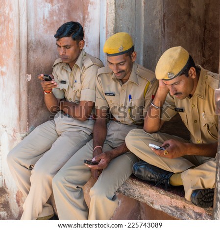Amber Fort, India - September 27, 2014: three police security sitting at the entrance of Amber fort playing with their mobile phones