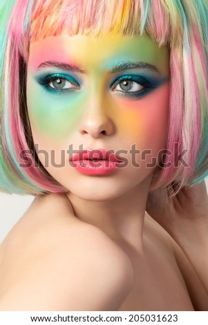 Portrait of young woman with funny rainbow colored make-up touching her hair