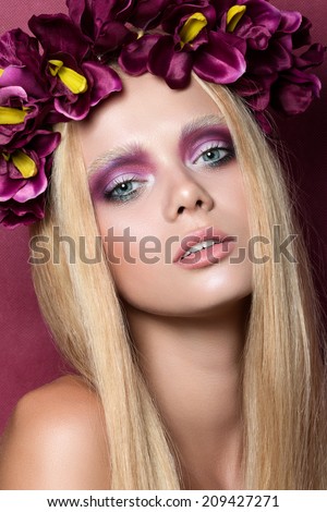 Beauty portrait of young blonde woman with purple floral wreath over red background