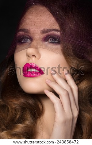 Portrait of young beautiful woman with brown curls and bright pink lips looking through purple veil