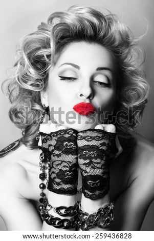 Retro styled black and white portrait of sexy adult playful woman with red lips blowing a kiss