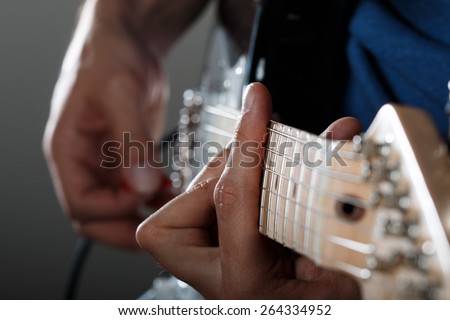 Hands of man playing electric guitar with red pick closeup