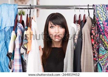 Portrait of young confused woman in front of a wardrobe full of clothes. Nothing to wear concept