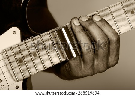 Hands of man playing electric guitar. Guitarist hands. Fingers with metallic slider pressing strings on maple fretboard closeup sepia tint. Old looking style.