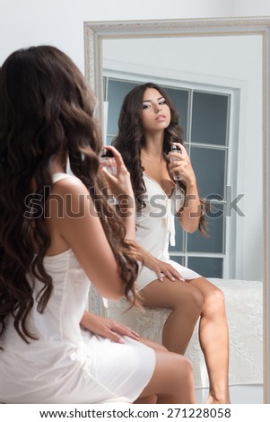 Young beautiful brunette woman sitting against mirror and applying perfume