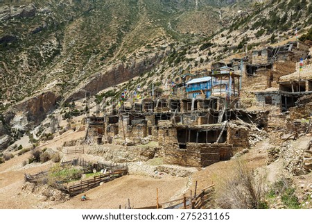 Stupa and a small blue hotel in the center of high mountain town Ghyaru. Local man doing some agricultural work near the town. Ghyaru, Himalayas, Nepal.