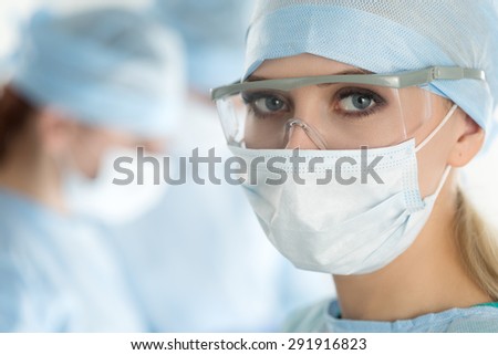 Close-up of surgeon woman looking at camera with colleagues performing in background in operation room