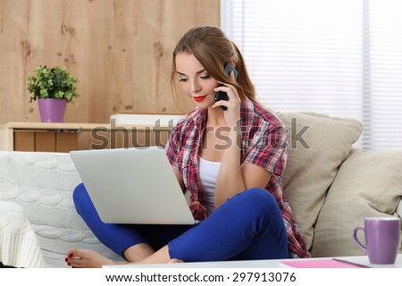 Young beautiful girl looking at notebook and calling to someone sitting on sofa at home