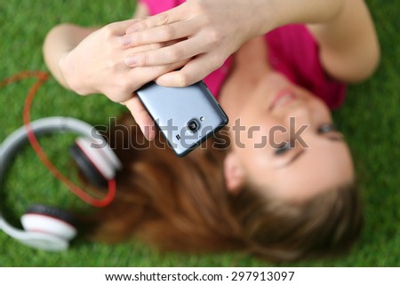 Young pretty girl taking self portrait with her smart phone laying on grass. Focus on phone
