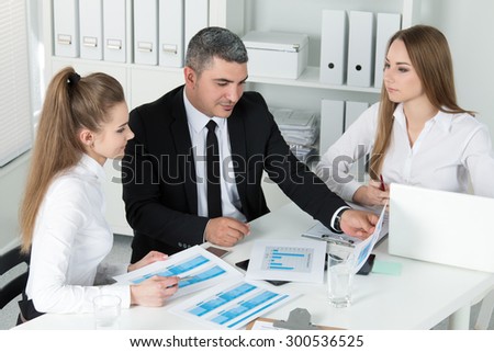 Two young beautiful business women consulting with their colleague. Partners discussing documents and ideas