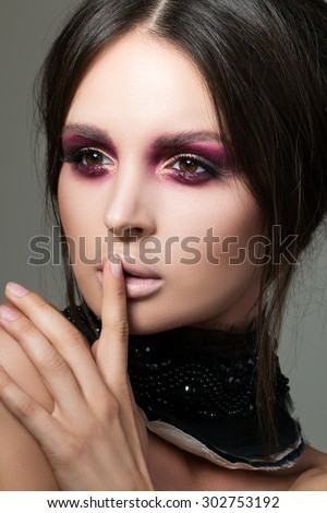 Close-up portrait of beautiful brunette woman with modern fashion make up making shh sign with her finger. Beauty, secrecy and fashion concept.