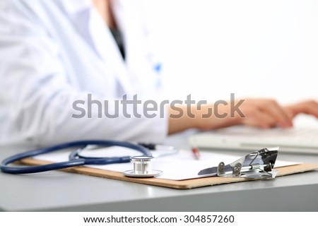 Medicine doctor\'s working place. Focus on stethoscope, doctor\'s hands typing something on background. Healthcare and medical concept. Copyspace