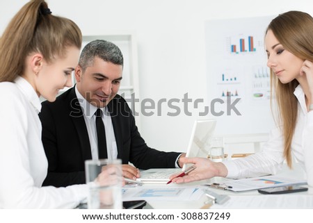 Adult businessman consulting his young female colleagues during business meeting. Partners discussing documents and ideas