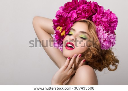 Close-up beauty portrait of young pretty girl with flowers in her hair wearing bright pink lipstick, touching her face. Bright modern summer makeup. Beauty, spa, hair styling and skincare concept