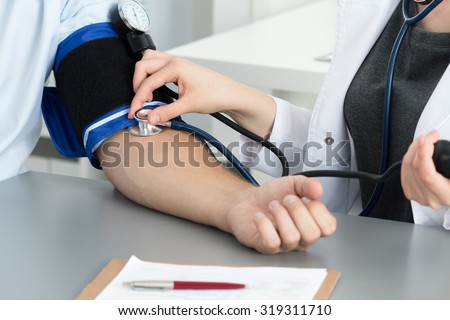 Female medicine doctor measuring blood pressure to her patient. Hands close up. Medical and healthcare concept