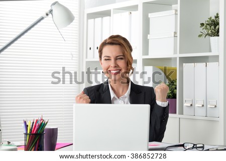 Portrait of happy young successful businesswoman celebrate something with arms up. Happy woman sit at office and look at laptop. Positive emotion. Big deal, promotion, lottery win or discount concept