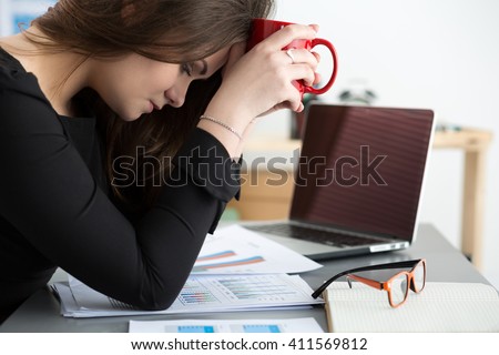 Tired female employee at workplace in office holding cup of tea. Sleepy worker early in the morning after late night work. Overworking, making mistake, stress, termination or depression concept