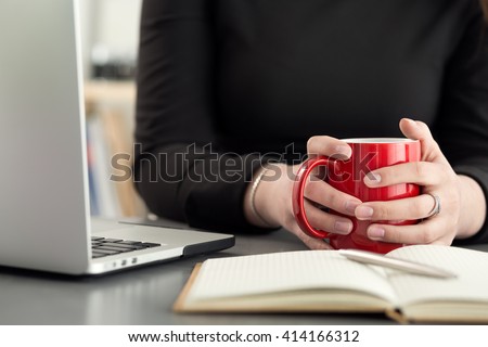 Female designers in office drinking morning tea or coffee. Coffeebreak during hard working day. Girl holding cup of hot beverage.