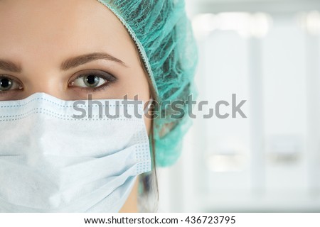Close-up portrait of young female surgeon doctor or intern wearing protective mask and hat. Healthcare, medical education, emergency medical service, surgery or veterinary concept