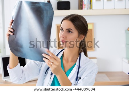 Young female medical doctor or intern looking at lungs x ray image standing at her office. Radiology, healthcare, medical service or education concept.