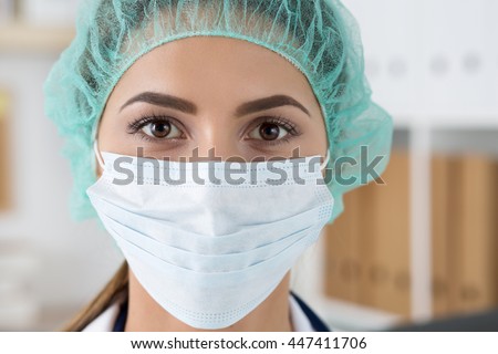 Close up portrait of young female surgeon doctor or intern wearing protective mask and hat. Healthcare, medical education, emergency medical service, surgery or veterinary concept