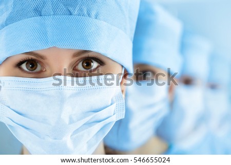 Close up portrait of young female surgeon doctor surrounded by her team. Group of surgeon in operation theatre. Healthcare, medical education, emergency medical service and surgery concept