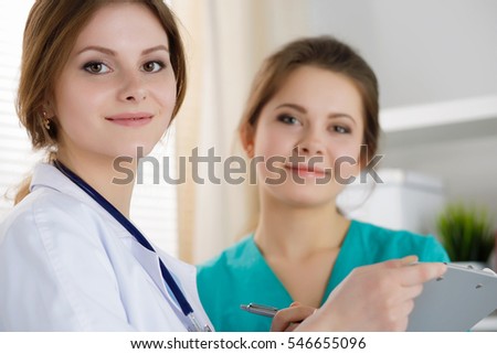 Two beautiful female medicine doctors working at their office discussing diagnose and filling patient registration or medical history form. Medical service, education, therapy and healthcare concept