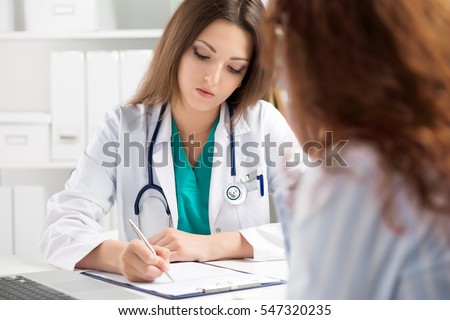 Doctor filling medical form while patient consultation. Patient sitting at doctor office. Diagnostic and prevention of women diseases, healthcare and medical service concept