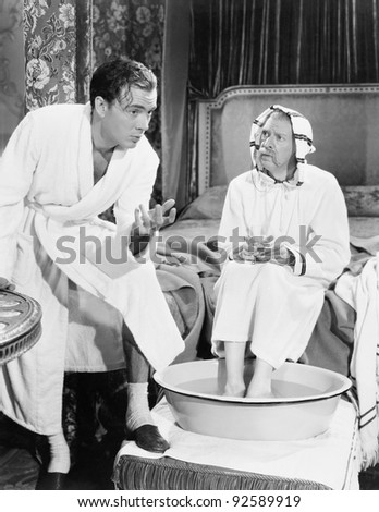 Young man talking to a senior man sitting with his feet soaked in a washtub