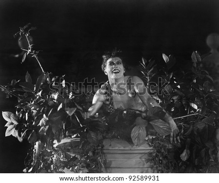 Portrait of a young man sitting on a wall with lowers and plants and smiling