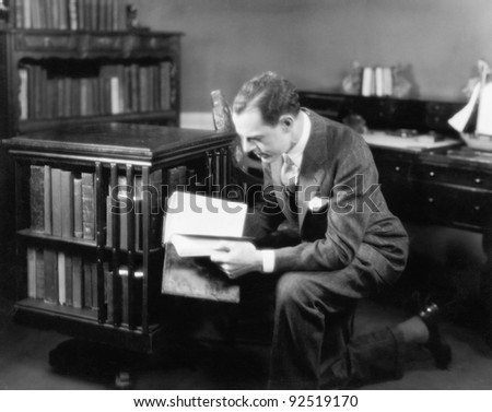 Man kneeling in his home library browsing a book