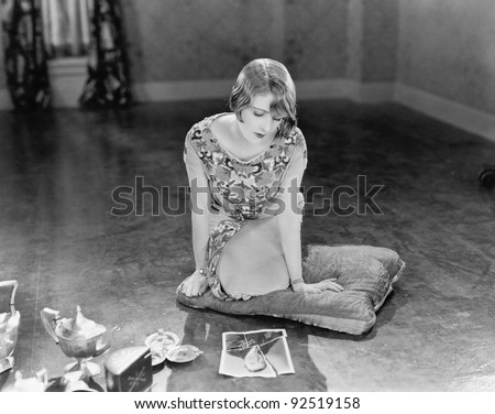 Woman kneeling on a pillow looking at a torn picture of a man