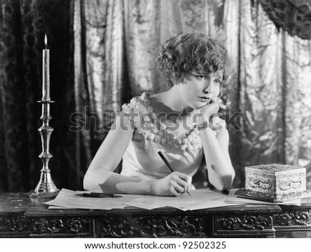 Young woman sitting at a desk with a pen in hand, looking sad while writing a letter