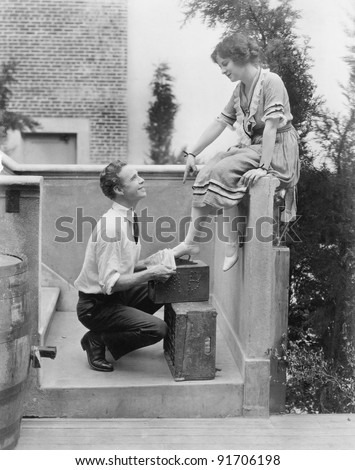 Woman sitting on a ledge having her shoes cleaned by a man