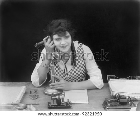 Young woman sitting at her desk in an office with a telephone in her hands
