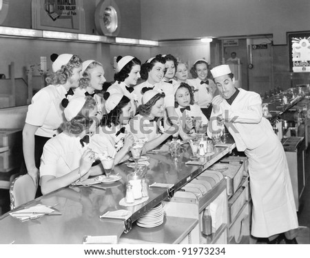 Young man surrounded by a group of college women in his soda fountain