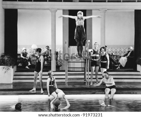 Young woman standing on a diving board surrounded by a group of people playing